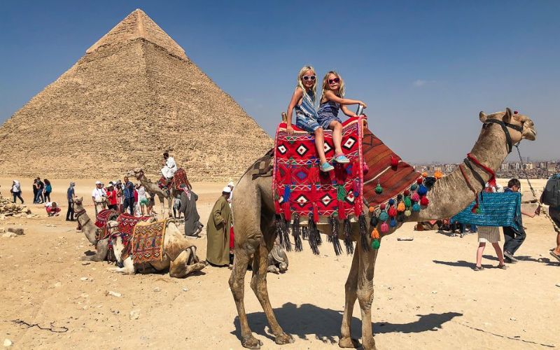 two-kids-riding-a-camel-around-the-pyramids-of-giza